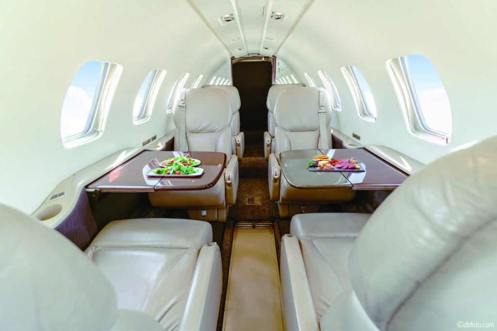 Cessna Citation Bravo cabin with cream leather club seats and wood worktables set with food, looking aft